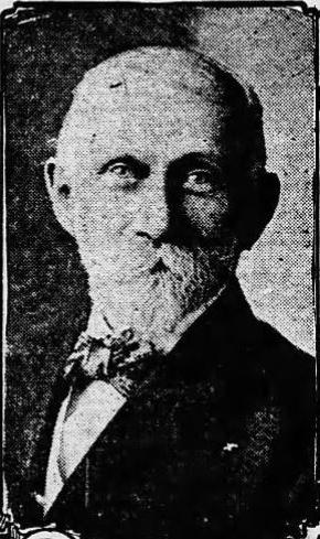 Black and white photograph of a white man with short gray hair, a mustache, and a beard wearing a black suit and a bowtie.